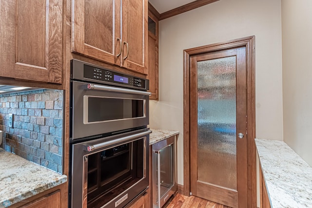 kitchen with backsplash, light hardwood / wood-style floors, stainless steel double oven, and crown molding