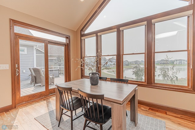 dining room featuring light wood-type flooring, vaulted ceiling, and a water view