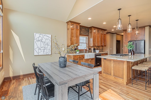 kitchen with appliances with stainless steel finishes, light stone counters, a kitchen island, pendant lighting, and light wood-type flooring