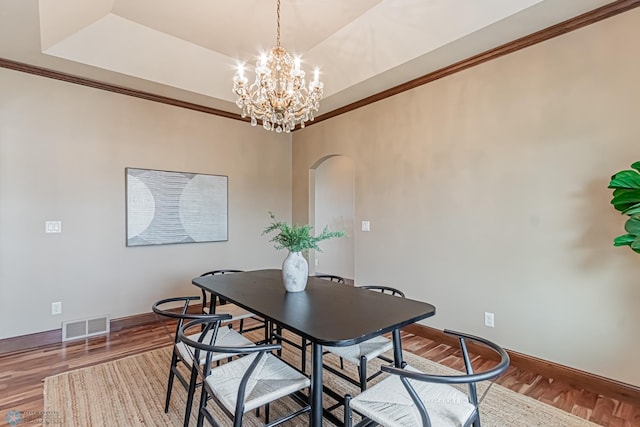 dining room with ornamental molding, hardwood / wood-style flooring, a raised ceiling, and a chandelier