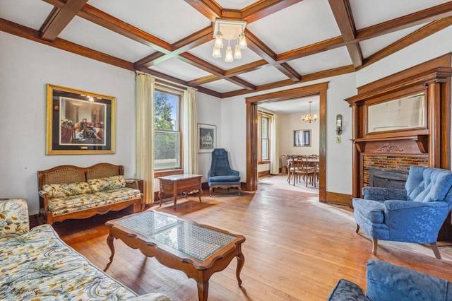 living room featuring coffered ceiling, a fireplace, beamed ceiling, an inviting chandelier, and light hardwood / wood-style flooring