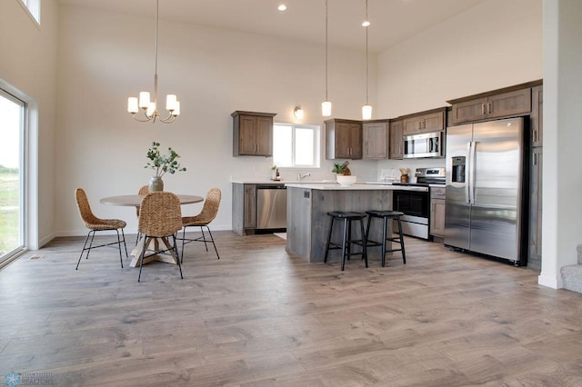 kitchen featuring pendant lighting, a chandelier, appliances with stainless steel finishes, a towering ceiling, and light hardwood / wood-style floors