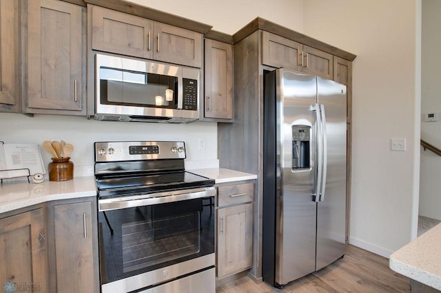 kitchen with light stone counters, appliances with stainless steel finishes, and light hardwood / wood-style floors