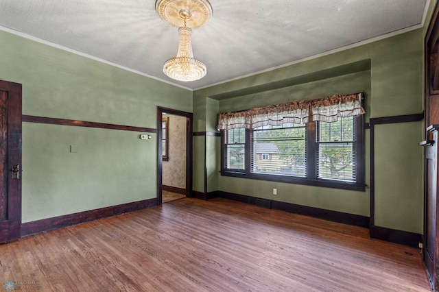 empty room featuring a textured ceiling, crown molding, a notable chandelier, and hardwood / wood-style flooring