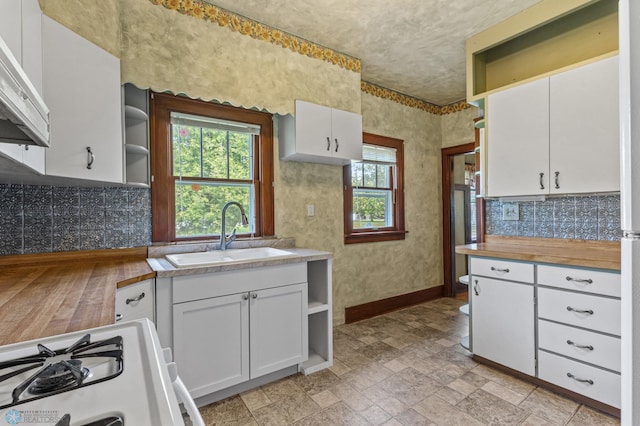 kitchen with a wealth of natural light, white gas stove, sink, white cabinetry, and exhaust hood