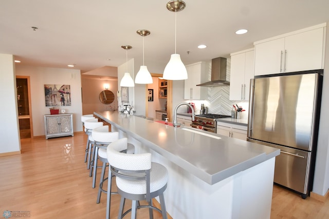 kitchen featuring sink, white cabinetry, wall chimney exhaust hood, stainless steel appliances, and decorative light fixtures