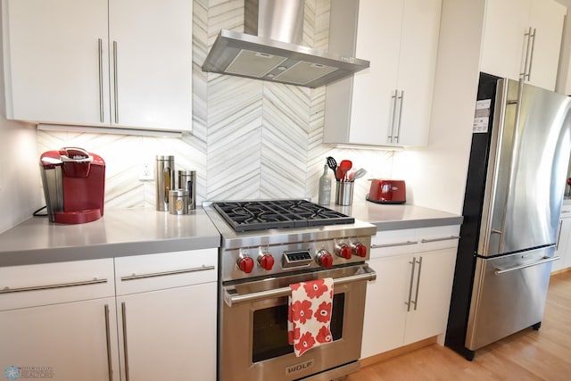 kitchen featuring white cabinets, backsplash, wall chimney range hood, stainless steel appliances, and light wood-type flooring