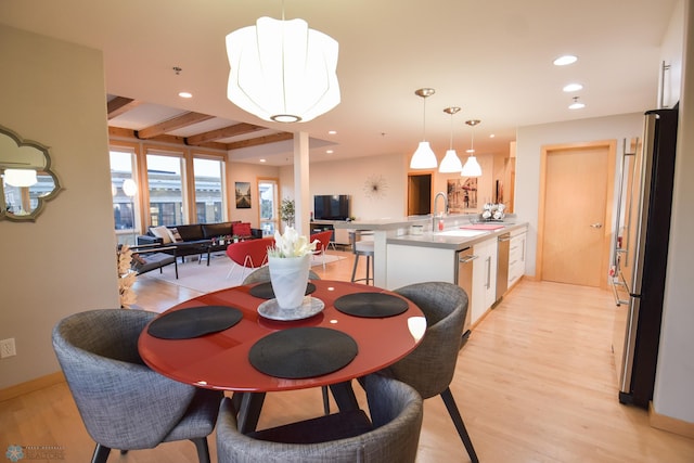 dining space featuring beamed ceiling, sink, and light hardwood / wood-style floors