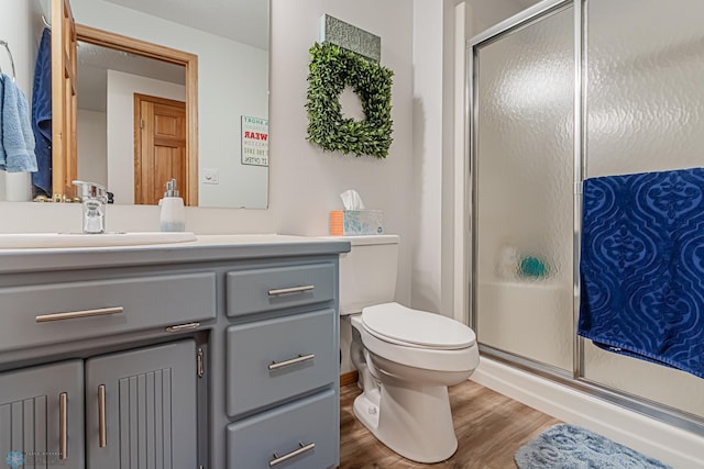 bathroom with wood-type flooring, a shower with door, vanity, and toilet