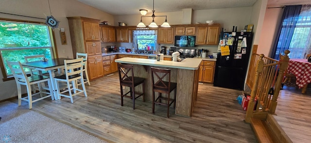 kitchen with hanging light fixtures, a kitchen island, light wood-type flooring, vaulted ceiling, and black appliances