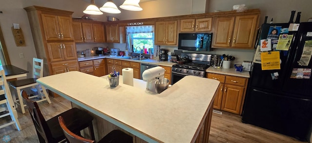 kitchen featuring black appliances, sink, a kitchen island, decorative light fixtures, and light hardwood / wood-style flooring