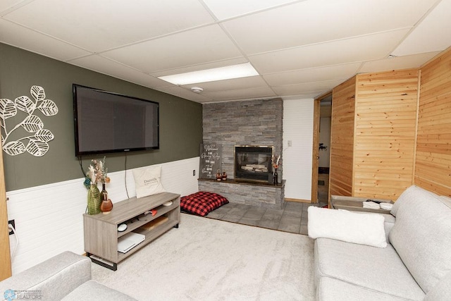 carpeted living room with wooden walls, a fireplace, and a paneled ceiling