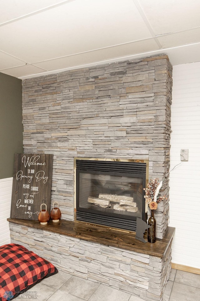 interior details featuring a paneled ceiling, a stone fireplace, and tile patterned floors