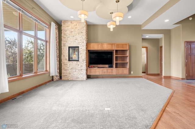 unfurnished living room with an inviting chandelier, a stone fireplace, and hardwood / wood-style flooring