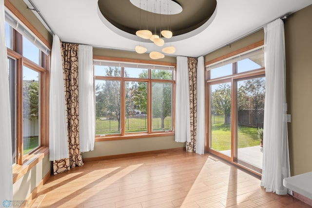 doorway to outside featuring a tray ceiling, a chandelier, light hardwood / wood-style flooring, and plenty of natural light