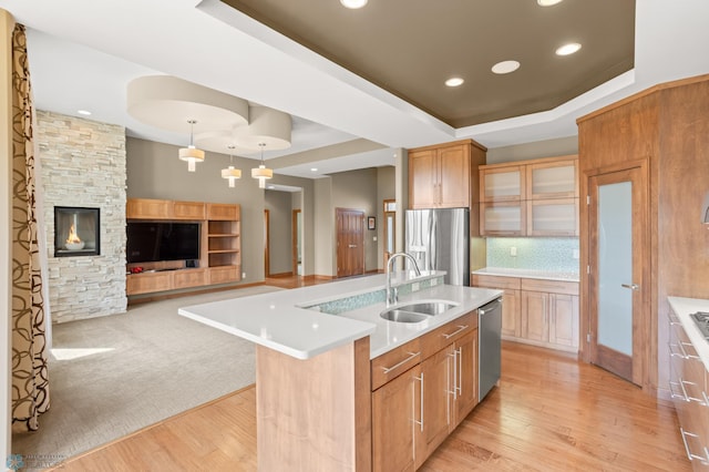 kitchen featuring appliances with stainless steel finishes, light hardwood / wood-style floors, decorative light fixtures, a center island with sink, and sink