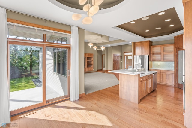 kitchen featuring decorative light fixtures, a kitchen island with sink, a tray ceiling, and light hardwood / wood-style flooring