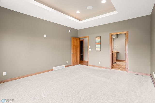 unfurnished bedroom with ensuite bath, a raised ceiling, and light colored carpet