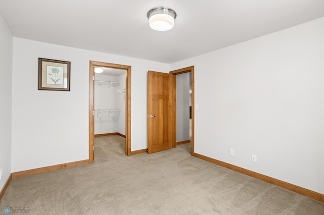 unfurnished bedroom featuring light carpet, a walk in closet, and a closet