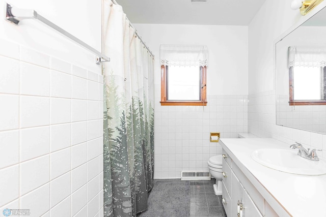 bathroom with tile walls, a wealth of natural light, vanity, and toilet