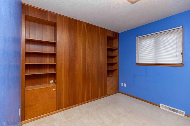 unfurnished bedroom featuring a textured ceiling, wood walls, and light colored carpet