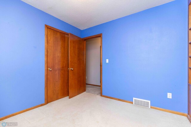 unfurnished bedroom featuring a textured ceiling, light colored carpet, and a closet