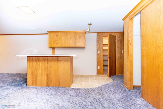 kitchen with light colored carpet, wood walls, ornamental molding, and kitchen peninsula