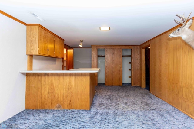 kitchen with crown molding, kitchen peninsula, wooden walls, and light colored carpet