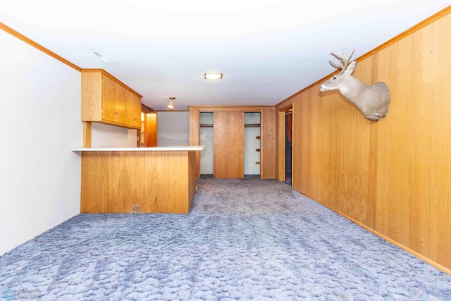 kitchen with ornamental molding, wooden walls, carpet, and kitchen peninsula