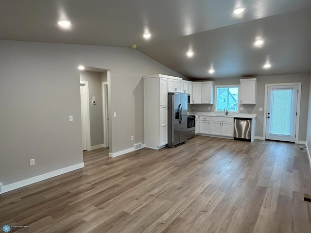 kitchen with appliances with stainless steel finishes, white cabinetry, light wood-type flooring, lofted ceiling, and sink