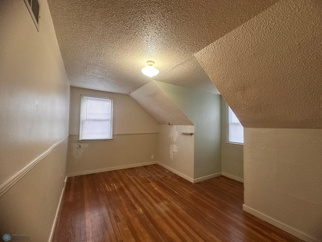 additional living space with vaulted ceiling, a textured ceiling, dark wood-type flooring, and a wealth of natural light