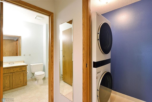 laundry area with a textured ceiling, stacked washing maching and dryer, and sink