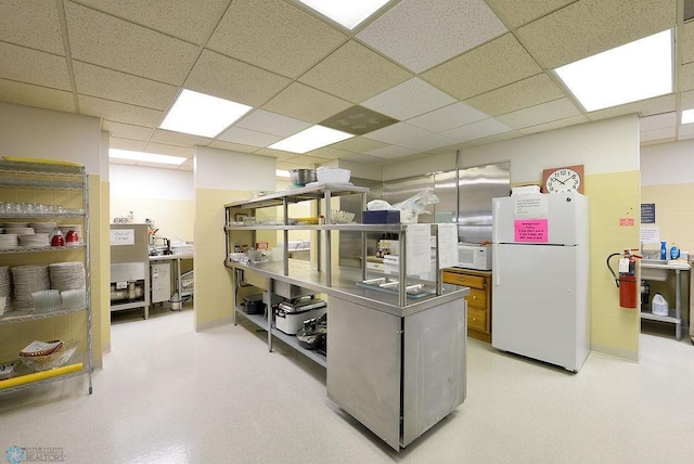 kitchen featuring stainless steel counters, a drop ceiling, and white appliances