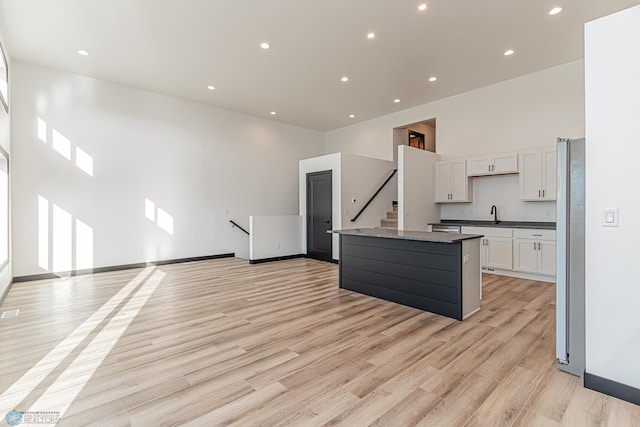 kitchen with white cabinets, stainless steel fridge, a center island with sink, light hardwood / wood-style flooring, and a towering ceiling