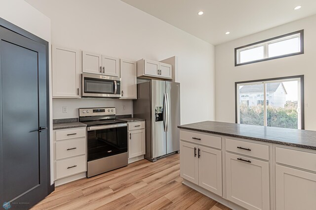 kitchen with dark stone countertops, stainless steel appliances, light hardwood / wood-style floors, and white cabinetry