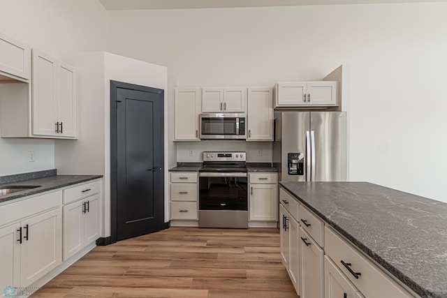 kitchen featuring stainless steel appliances, white cabinetry, light hardwood / wood-style floors, and dark stone countertops