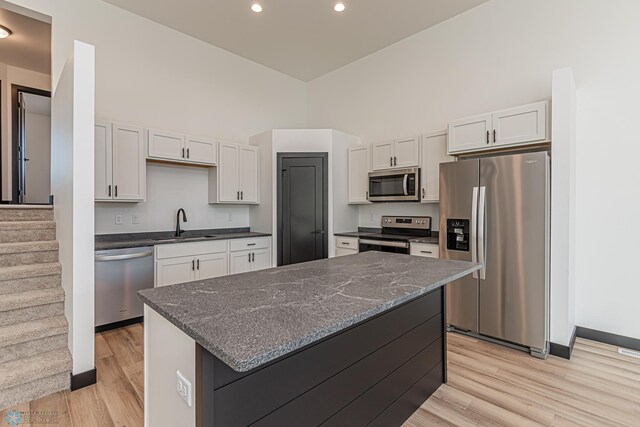 kitchen with white cabinets, a kitchen island, appliances with stainless steel finishes, dark stone countertops, and light wood-type flooring