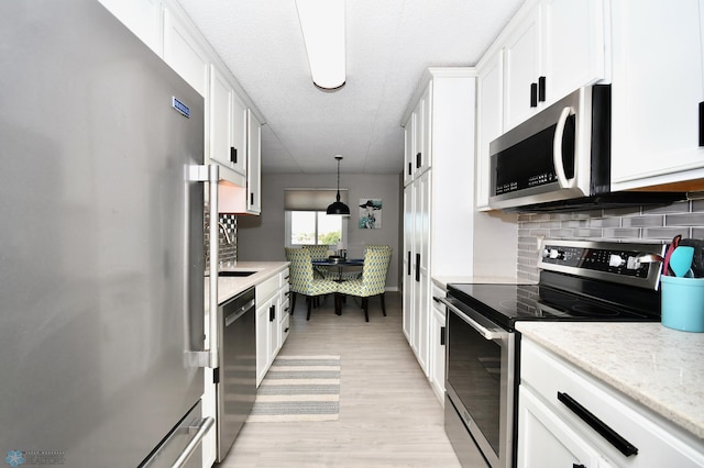 kitchen featuring white cabinets, hanging light fixtures, light hardwood / wood-style flooring, appliances with stainless steel finishes, and decorative backsplash