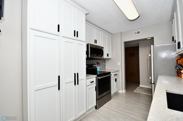 kitchen with light stone counters, white cabinets, light hardwood / wood-style flooring, appliances with stainless steel finishes, and decorative backsplash