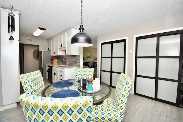 dining area with a textured ceiling, sink, and light hardwood / wood-style flooring