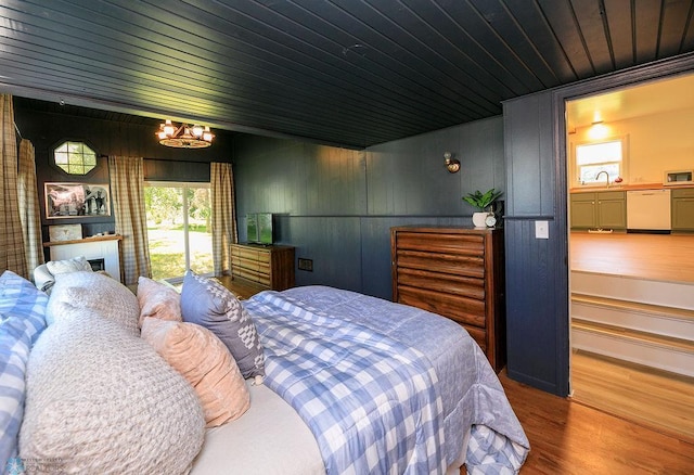 bedroom with wood walls, hardwood / wood-style flooring, wooden ceiling, a notable chandelier, and a fireplace