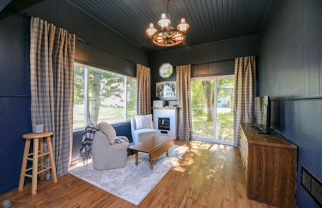 living area with an inviting chandelier, light wood-type flooring, wooden ceiling, and wooden walls