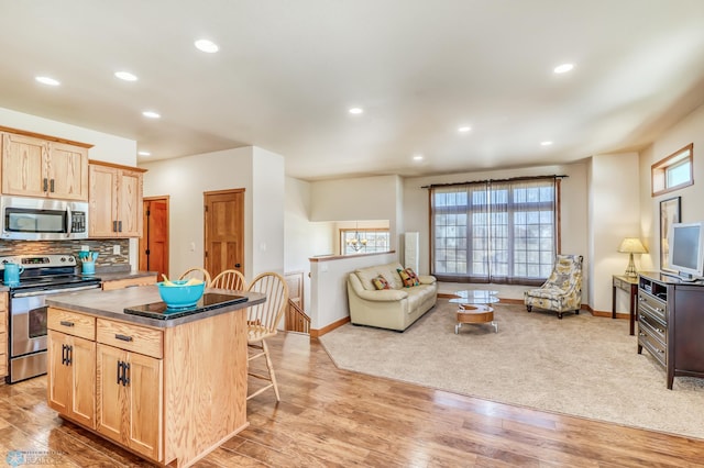 kitchen featuring light brown cabinets, stainless steel appliances, a center island, a breakfast bar area, and light hardwood / wood-style floors