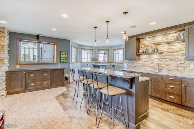 kitchen with light wood-type flooring, a breakfast bar area, a kitchen island, decorative light fixtures, and light stone countertops