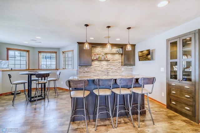 kitchen featuring dark brown cabinets, light stone counters, light hardwood / wood-style floors, a breakfast bar area, and hanging light fixtures