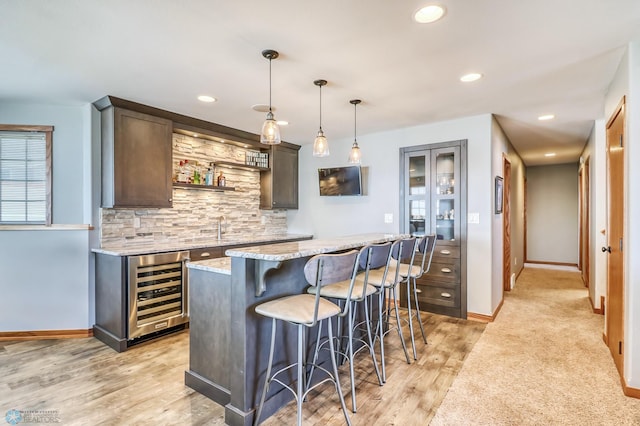 kitchen with light stone counters, dark brown cabinets, beverage cooler, light hardwood / wood-style flooring, and a center island