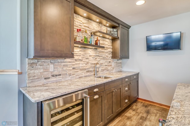 bar featuring sink, tasteful backsplash, beverage cooler, light hardwood / wood-style flooring, and light stone countertops