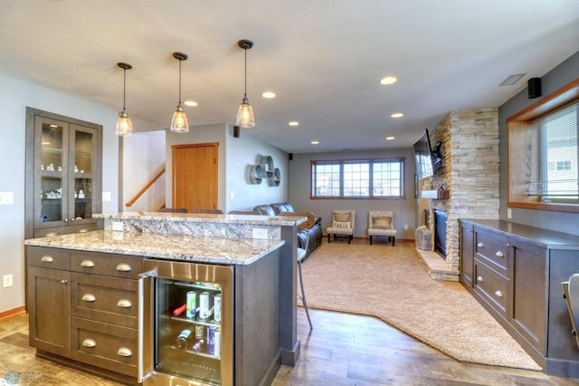 kitchen featuring wine cooler, light hardwood / wood-style floors, a kitchen bar, decorative light fixtures, and a stone fireplace