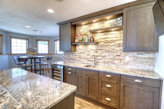 kitchen with beverage cooler, light stone counters, light hardwood / wood-style floors, and sink