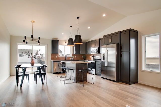 kitchen featuring a center island, lofted ceiling, a kitchen bar, appliances with stainless steel finishes, and decorative light fixtures